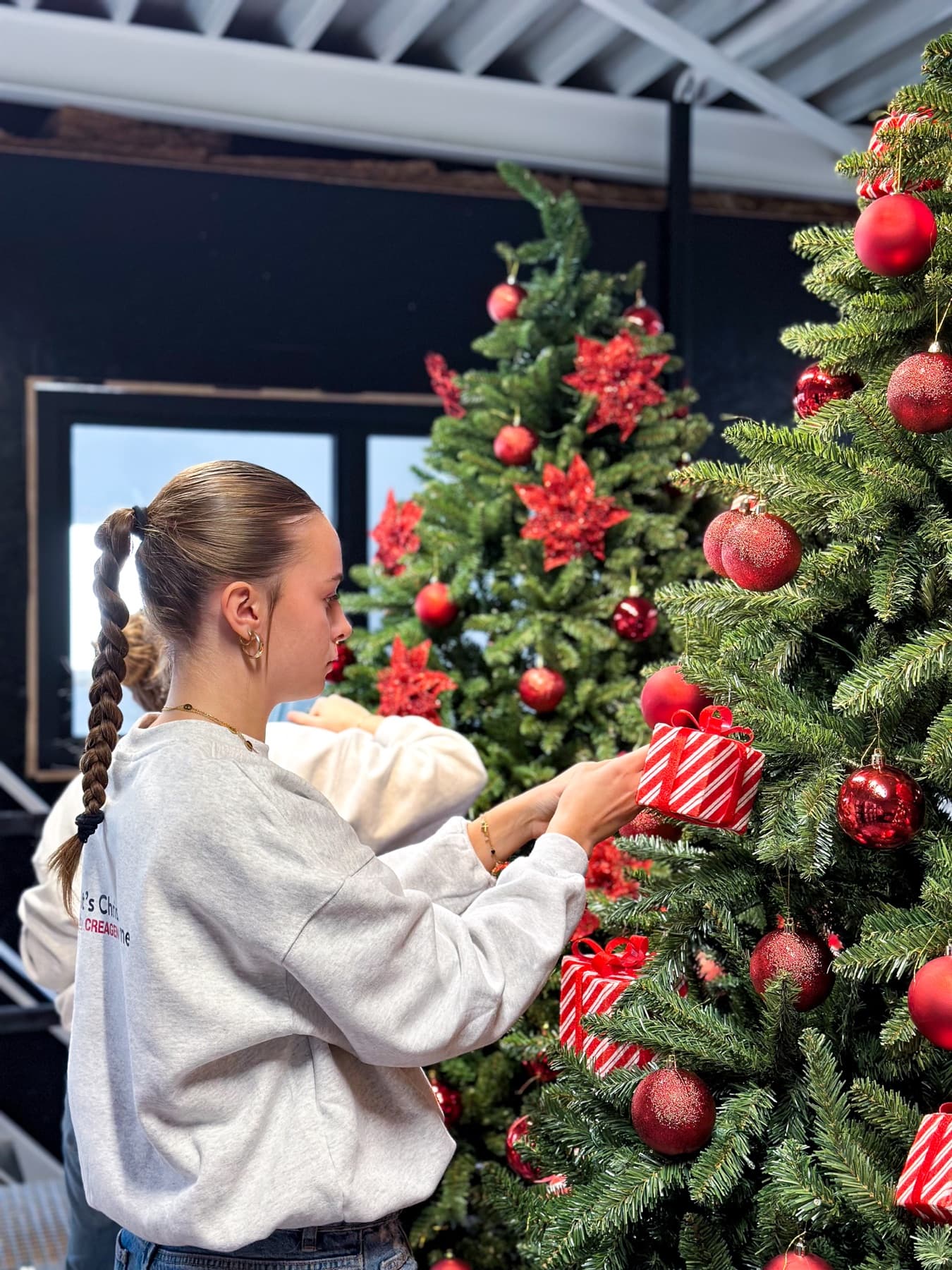 Une décoratrice place un ornement cadeau sur un sapin rouge