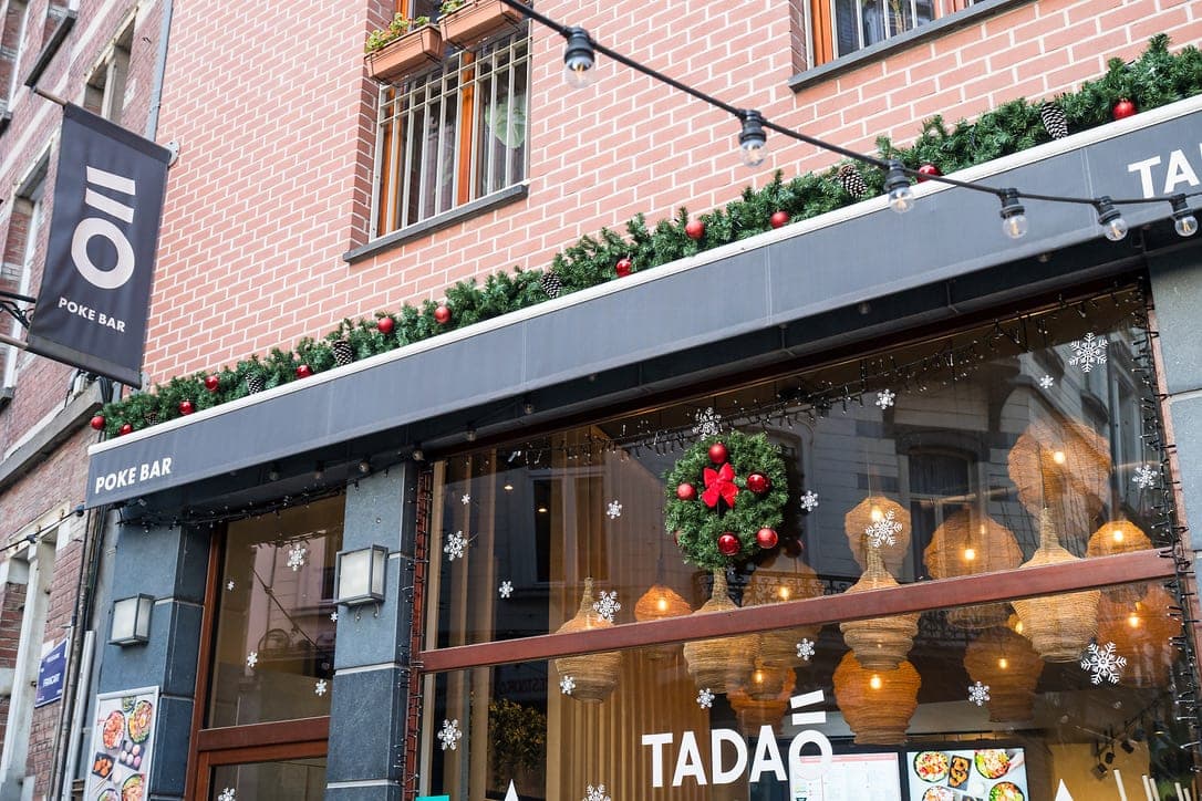 Façade de Noël Tadao à Ixelles avec guirlande de sapin, couronne et vitrophanie, 2025